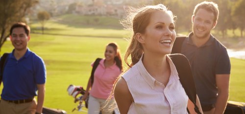 Group Of Golfers Walking Along Fairway Carrying Golf Bags